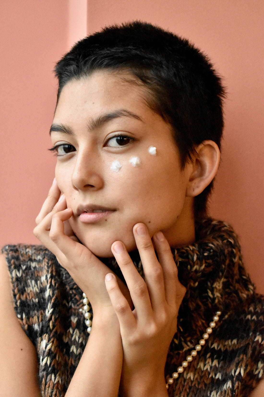 A young woman with 3 dots of cream on her face.