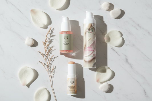 B's Botanicals peptide skincare beginner routine — Peptide Anti-Aging Serum, Peptide Ageless AM/PM Cream with Hyaluronic Acid, and SPF50 Tinted Stick arranged on white marble with magnolia petals — COSMOS Natural certified skincare products