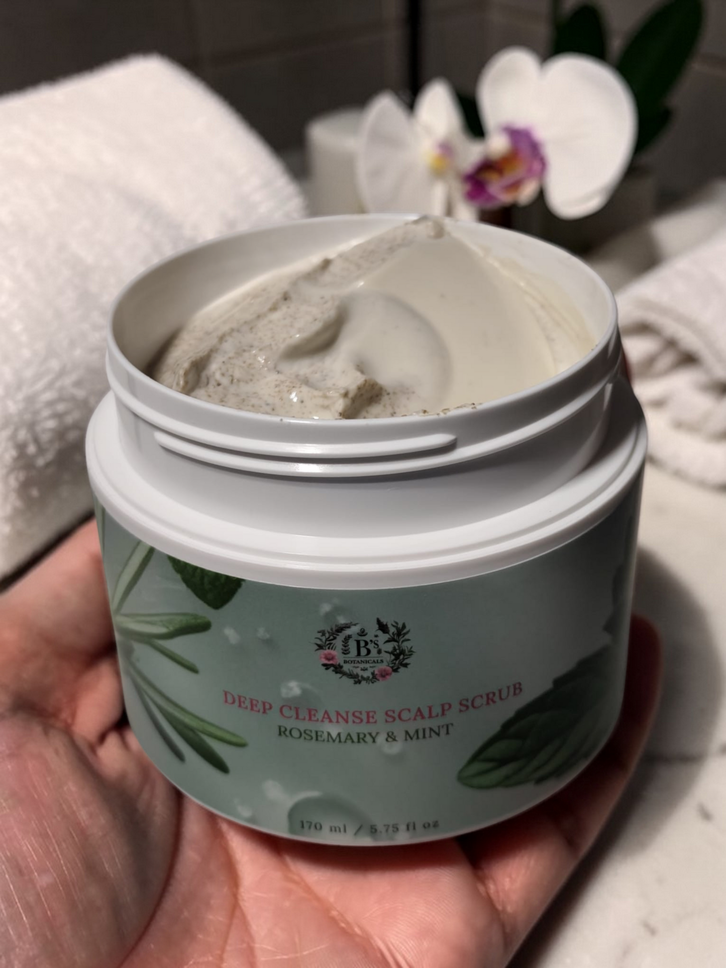 Deep Cleanse Scalp Scrub with Rosemary and Mint for invigorating and exfoliating scalp care in a bathroom held in hand.
