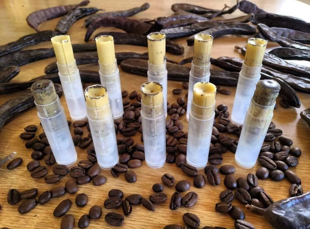 Clear lip balm tubes with yellow caps on a wooden surface with coffee beans and coffee beans.