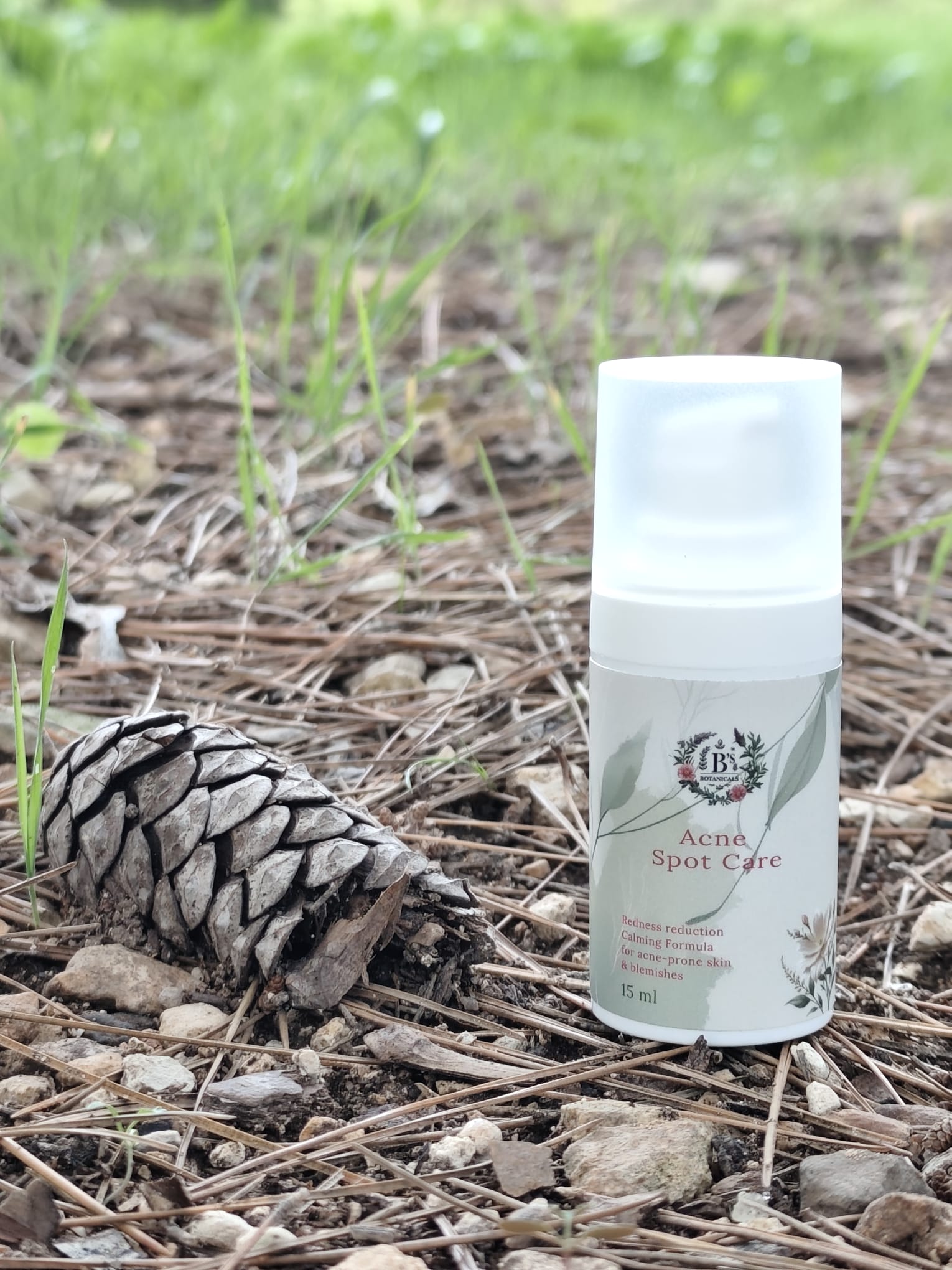 Skincare product labeled 'Acne Spot Care' on a natural background with grass and pine cone.